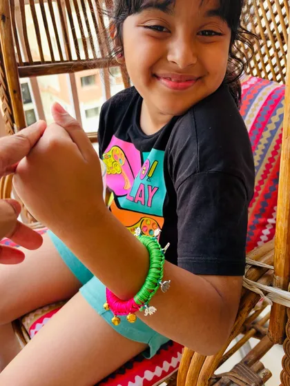 I designed this jingly bangle especially for kids. It's a wooden base wrapped in bright satin ribbon, with tiny golden ghungroos and little haathi charms that make a happy sound with every movement.