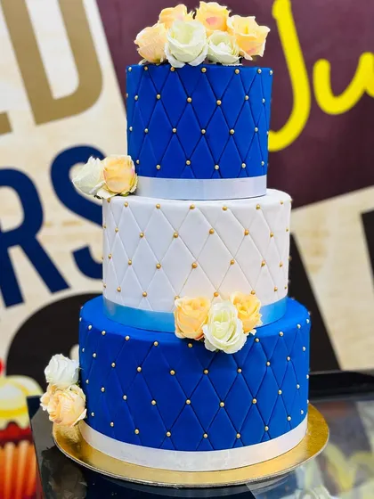 We love creating elegant designs like this 7kg, three-tiered cake. It features a sophisticated royal blue and white fondant with a quilted pattern, gold bead detailing, and is topped with beautiful handmade sugar roses, perfect for weddings, anniversaries, or grand birthday celebrations.