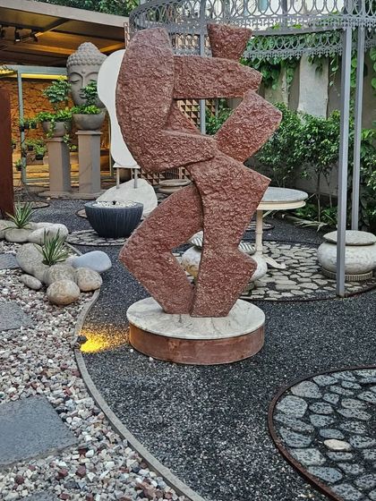 This abstract stone sculpture adds a dynamic and modern artistic element to a gravel and stone garden path.