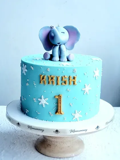 A sweet and simple first birthday cake with a sleeping baby elephant topper. The cake is decorated with fondant snowflakes for a "winter wonderland" feel.