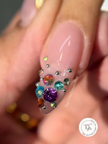 A macro shot of a jeweled accent nail, featuring a cascade of multi-colored rhinestones on a classic French tip.