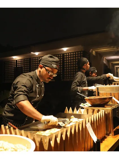 Our team of chefs works diligently at a long live station during an evening event. This shows our capacity to handle large crowds while maintaining our high standards of quality and presentation.