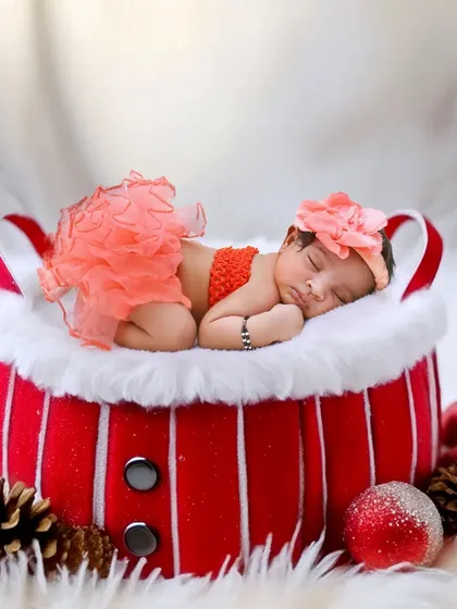 A festive Christmas-themed photo with a newborn sleeping in a Santa-style basket.
