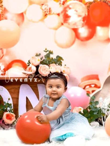For this cake smash session, I used a warm color palette with peach, pink, and white balloons. The setup includes a wooden 'ONE' block, floral arrangements, and other soft props to create a beautiful portrait of the birthday girl.