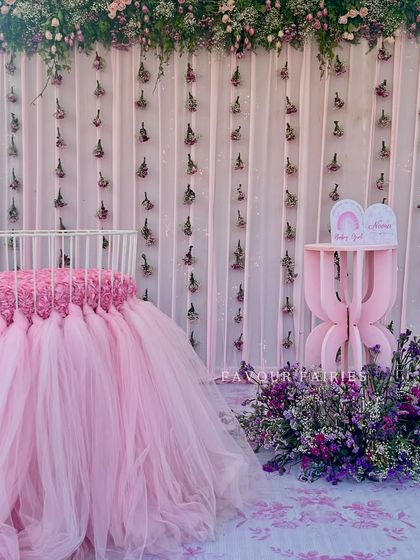 A beautiful setup for a baby girl's welcoming ceremony, featuring a cradle with a long pink tulle skirt and a backdrop of curtains with hanging flowers.