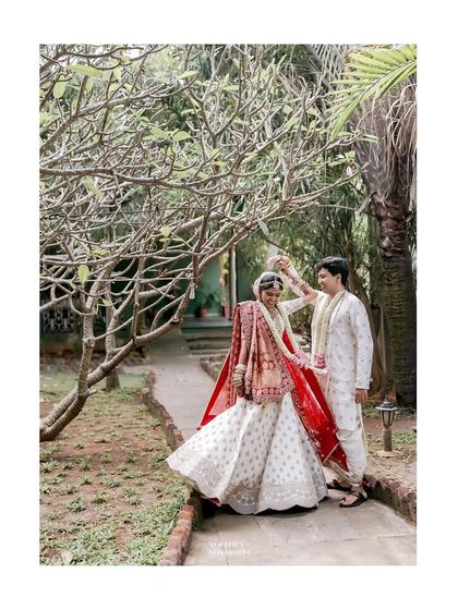 A couple enjoys a dance in a sunlit garden path, the bride's red veil flowing beautifully.