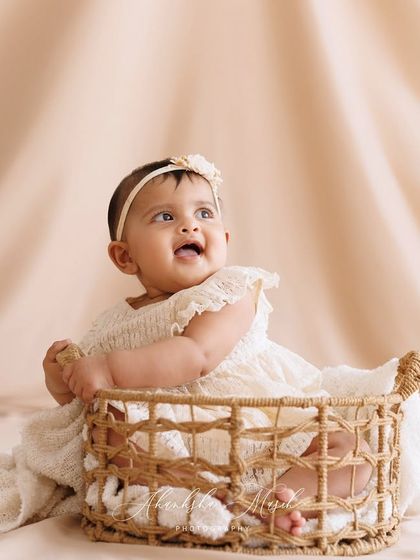 A perfect sitter session moment. This baby's happy, upward gaze and her placement in a simple wicker basket create a beautiful and classic portrait, capturing the joy of this milestone.
