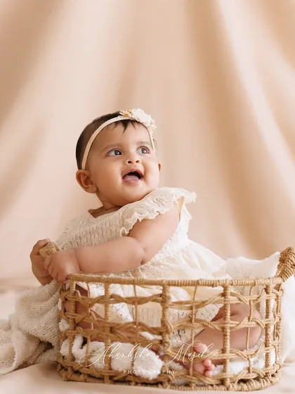 A perfect sitter session moment. This baby's happy, upward gaze and her placement in a simple wicker basket create a beautiful and classic portrait, capturing the joy of this milestone.