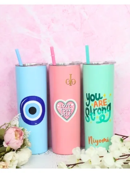 A trio of our personalized skinny tumblers in blue, pink, and mint. Each one is customized with a different design, including an evil eye, a "Love Your Self" heart, and a "You Are Strong" quote.