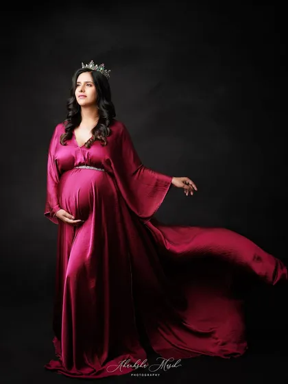 A regal pose in a flowing magenta satin gown and crown, looking off to the side with a sense of quiet power.