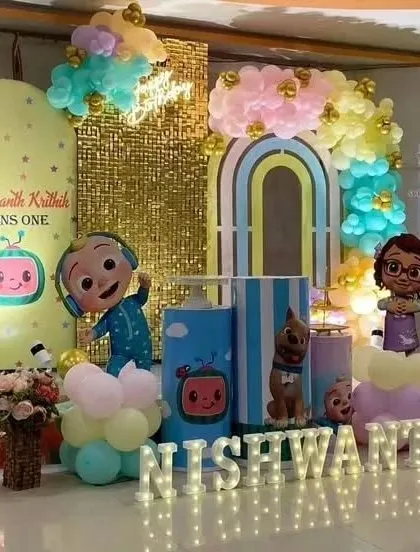 An elaborate Cocomelon first birthday setup with a gold sequin wall. This decoration features multiple themed backdrops, marquee letters, and pastel balloon arrangements.