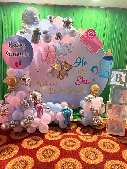 A "He or She" gender reveal backdrop with a "We can Bearly wait" theme. The setup includes a custom printed backdrop, a balloon garland in pink, blue, and silver, and transparent "BABY" blocks.
