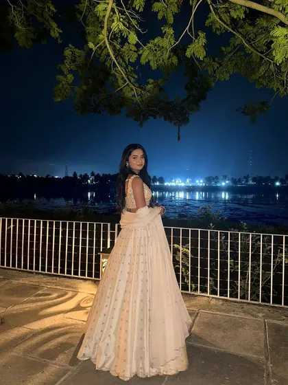 A beautiful client in an ivory lehenga, captured against a scenic backdrop at night.