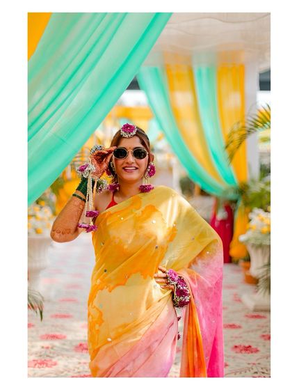 A stylish shot of the bride in her colourful saree and sunglasses, posing at her Haldi ceremony.