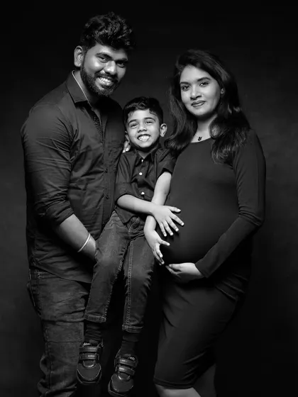 A timeless black and white family portrait. This classic studio shot focuses on the family's connection and joy, with the simple dark clothing and background ensuring that their expressions are the main story.