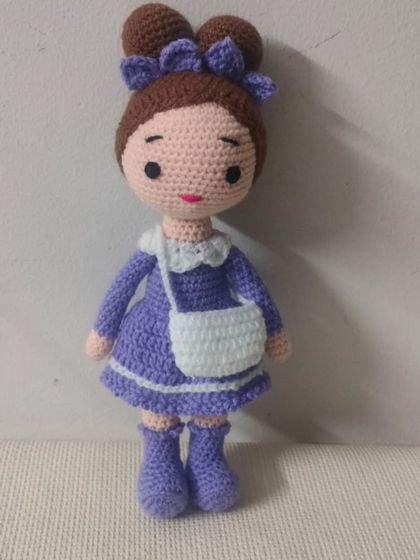 A lovely doll in a purple dress with a white lace collar. She also has a little white bag.