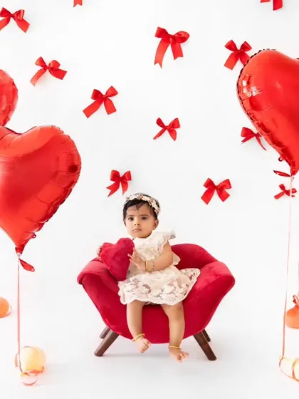 A full view of the Valentine's Day set, with a tiny baby seated in a red armchair surrounded by heart balloons.