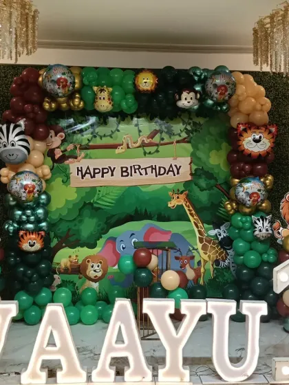 A full jungle-themed first birthday stage, with a lush green backdrop, various animal cutouts, and large marquee letters for the name "VAAYU".
