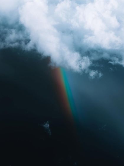 A fragment of a rainbow emerges from a dark, stormy cloud. Capturing these fleeting moments of light and weather is a key part of my landscape work.