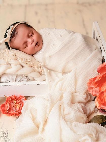 A peaceful portrait of a baby sleeping in a tiny white bed, surrounded by beautiful red flowers. The contrast between the soft whites and vibrant reds is stunning.