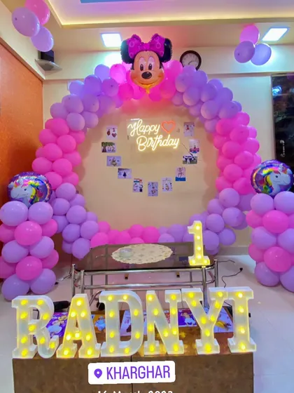 A Minnie Mouse themed first birthday party at home in Kharghar. The setup features a pink and purple circular balloon arch and marquee letters spelling 'Radnyi'.