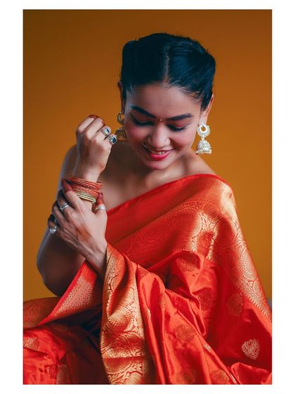 A moment of quiet reflection. This image captures the model in a beautiful orange saree, adjusting her bangles, with the focus on the rich fabric and traditional jewelry.
