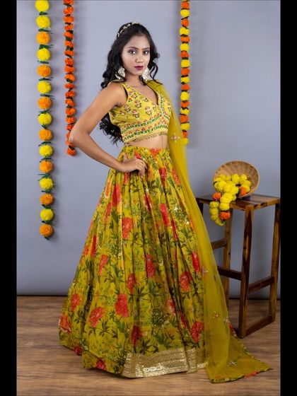 A full view of the mustard yellow lehenga with a beautiful red and green floral print. The embroidered blouse and sheer dupatta make it a perfect outfit for a haldi or mehendi ceremony.