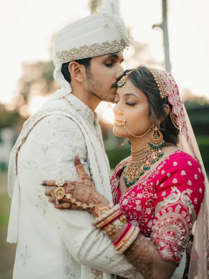 A golden hour portrait filled with warmth and love. The groom's tender forehead kiss and the soft sunlight create a truly magical and romantic image.
