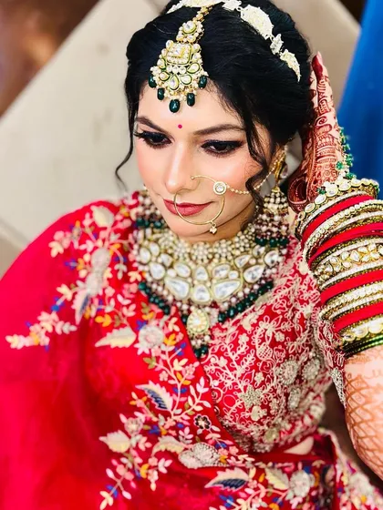 A close-up of a bride's stunning look. Her intricate jewelry, including the maang tikka and nose ring, is perfectly balanced with her bold eye makeup and red lehenga.