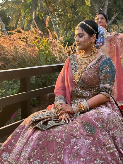 This bride is ready for her Goa wedding, sitting in the golden hour light. Her hair is styled in a beautiful braided bun with pastel-colored flowers, perfect for a beachside ceremony.