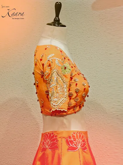 A side view of the orange blouse, highlighting the intricate zardosi and beadwork on the sleeve. This angle shows the depth and texture of the hand-embroidery.
