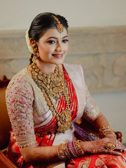 A portrait of a radiant South Indian bride, her hands adorned with a rich mehendi stain that complements her red silk saree.
