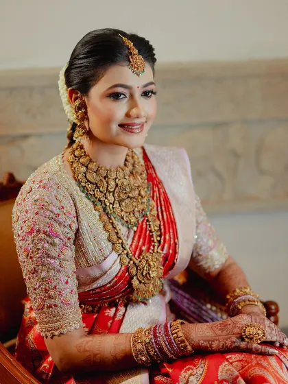 A portrait of a radiant South Indian bride, her hands adorned with a rich mehendi stain that complements her red silk saree.