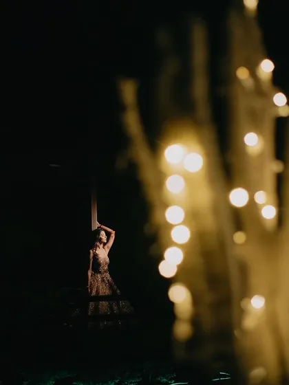 An artistic and creative shot using foreground elements. The blurred fairy lights create a dreamy, magical effect, framing the couple in the background and adding a sense of wonder to the portrait.