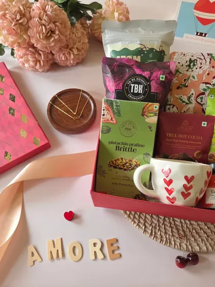 This "Amore" themed hamper is all about love. It features a heart-themed mug, pistachio praline brittle, and other gourmet treats, surrounded by flowers and a romantic ribbon.