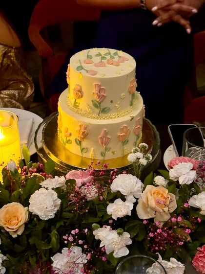 A beautiful two-tiered cake with delicate, hand-painted floral designs, sitting amongst a bed of fresh flowers. This is perfect for birthdays, anniversaries, or any intimate celebration.