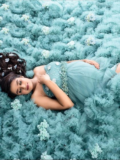 A dreamy, ethereal portrait created by having the client lie on a bed of soft, ruffled teal fabric. This overhead shot, adorned with small flowers, creates a unique and artistic 'sleeping beauty' effect.