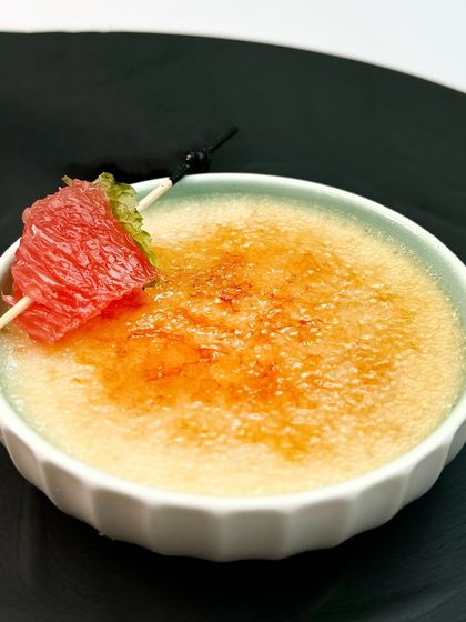 A close-up of the coconut and jaggery brulee, with a perfectly caramelized top and a garnish of ruby grapefruit for a pop of freshness.