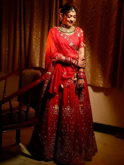 A full-length portrait of the bride in her red wedding lehenga, looking absolutely radiant.