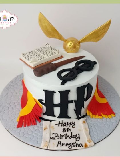 A magical Harry Potter cake for an 8th birthday. This cake is adorned with the Gryffindor scarf, Harry's glasses, a wand, a spellbook, and the Golden Snitch.