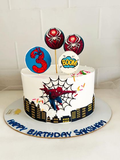 A clean and modern Spider-Man cake with a cityscape border and comic book-style toppers.