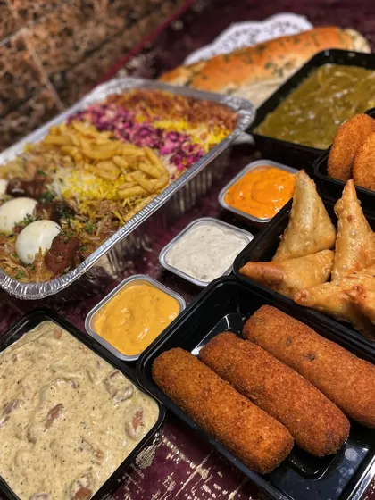 A close-up of the delicious components of my Iftar box. You can see the rich biryani, crispy samosas, savory rolls, and creamy curries, all packed neatly and ready for your celebration.