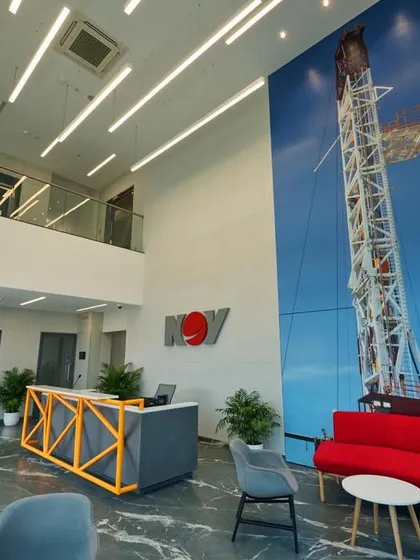 A double-height reception lobby for an engineering company. The design incorporates a massive graphic of an oil rig, reflecting the client's industry, and uses a bold red sofa for a splash of color.