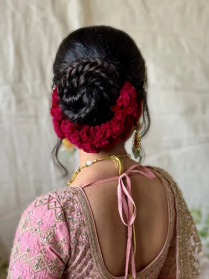 A unique and modern take on the bridal bun, featuring a braided detail and a vibrant red floral arrangement made of soft material. This is a bold and artistic choice.