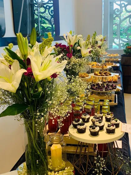 This wide shot shows a full dessert and beverage bar decorated with multiple fresh floral centerpieces. Coordinated arrangements across the entire station create a cohesive and high-end look for your corporate event's catering.