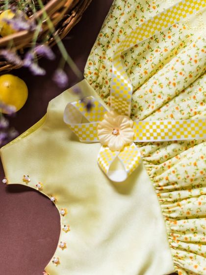 This detailed shot shows the hand-beaded neckline and the checkered and solid ribbon bow of this yellow dress, highlighting the care put into every element.