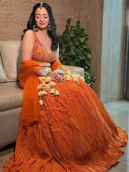 A full-length shot of the vibrant orange lehenga. The makeup is kept bright and fresh to match the festive mood of the event.