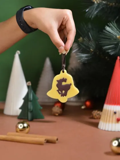 A yellow bell-shaped Christmas ornament featuring a reindeer silhouette. It brings a touch of rustic charm and festive fragrance to your tree.