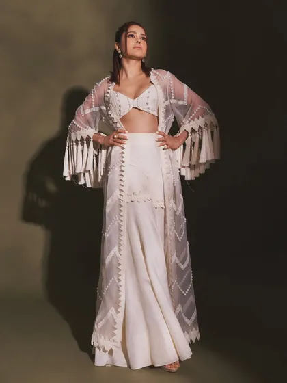 Pearls and tassels make this white indo-western outfit on Nushrratt Bharuccha truly special. The fringed jacket adds a playful, bohemian touch to the elegant sharara set.