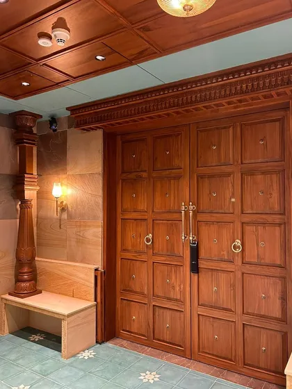 The entrance to the Embassy Lake Terraces residence sets a grand and traditional tone. A massive, intricately detailed wooden door is flanked by a carved pillar and a stone-clad wall, immediately signaling the home's unique blend of heritage and luxury.